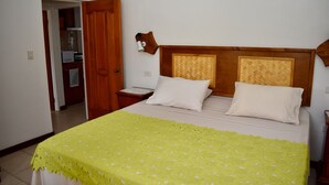 A bedroom with a bed, two pillows, a nightstand, a wooden headboard, and a wall-mounted lamp. - Aito1 across from Muri Beach (Muri Beach)