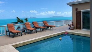 A pool area with lounge chairs and a view of the ocean.