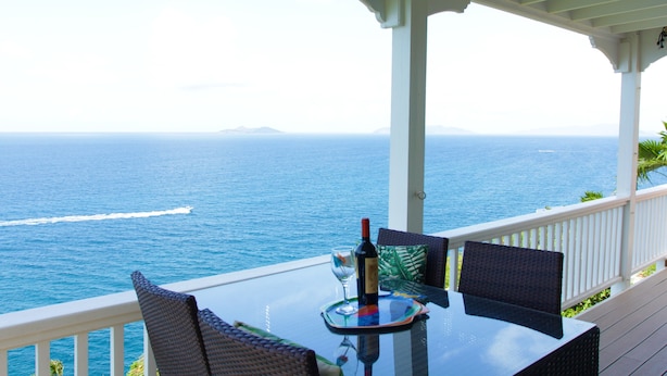 A glass table with chairs on a balcony overlooking the ocean.