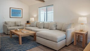 A living room with a beige sectional sofa, two wooden coffee tables, and a framed picture on the wall. - Beach Please ~ Luxe Cottage ~ Steps from Sand (Treasure Island)