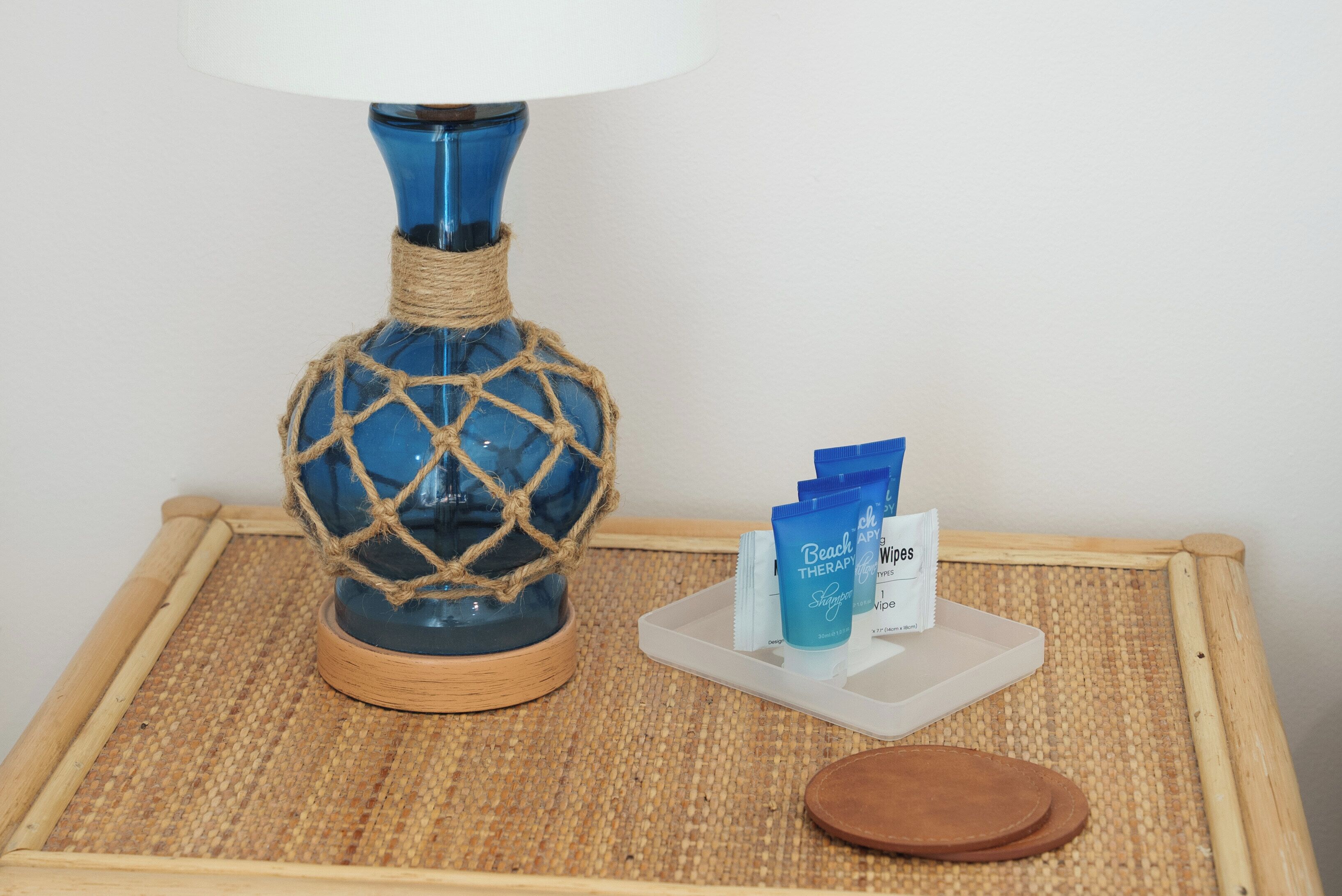 A blue glass bottle with a rope net, a tray with skincare products, and a wooden tray.