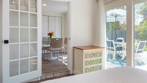 A bedroom with a large bed, a glass door leading to a patio with outdoor furniture and a pool. - Beach Please ~ Luxe Cottage ~ Steps from Sand (Treasure Island)