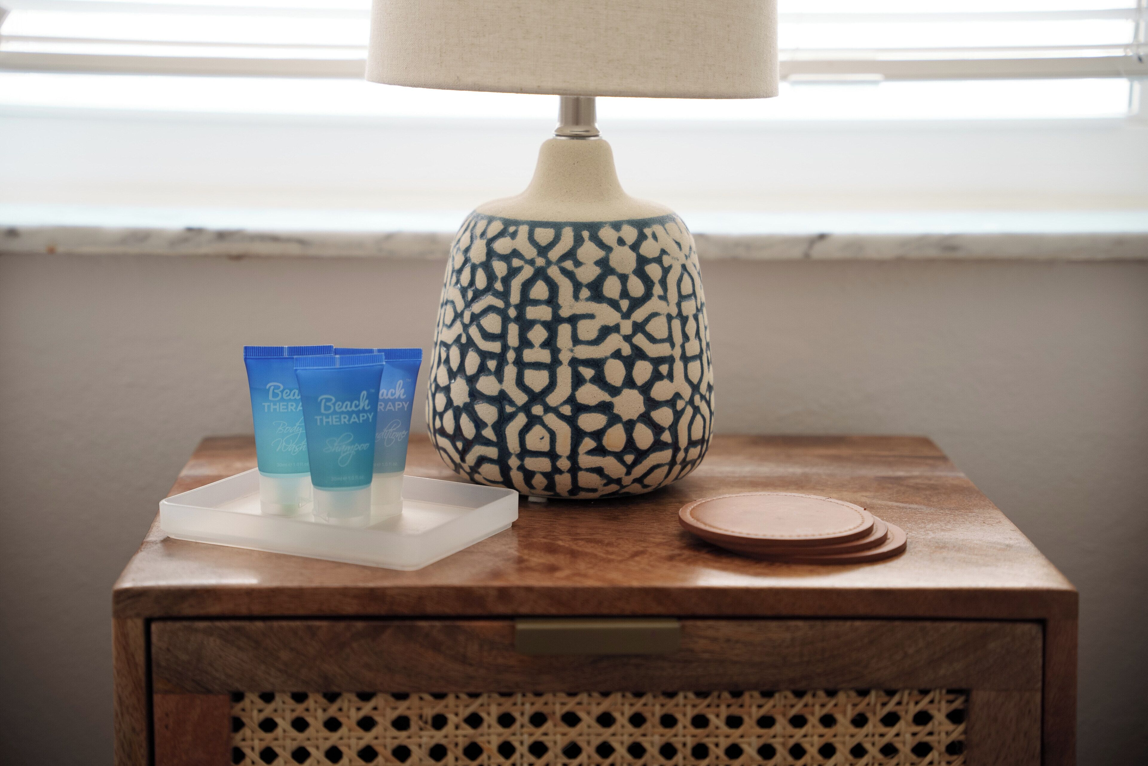 Ein Nachttisch aus Holz mit einer Lampe, einem Tablett mit zwei blauen Flaschen und einer verzierten Vase.