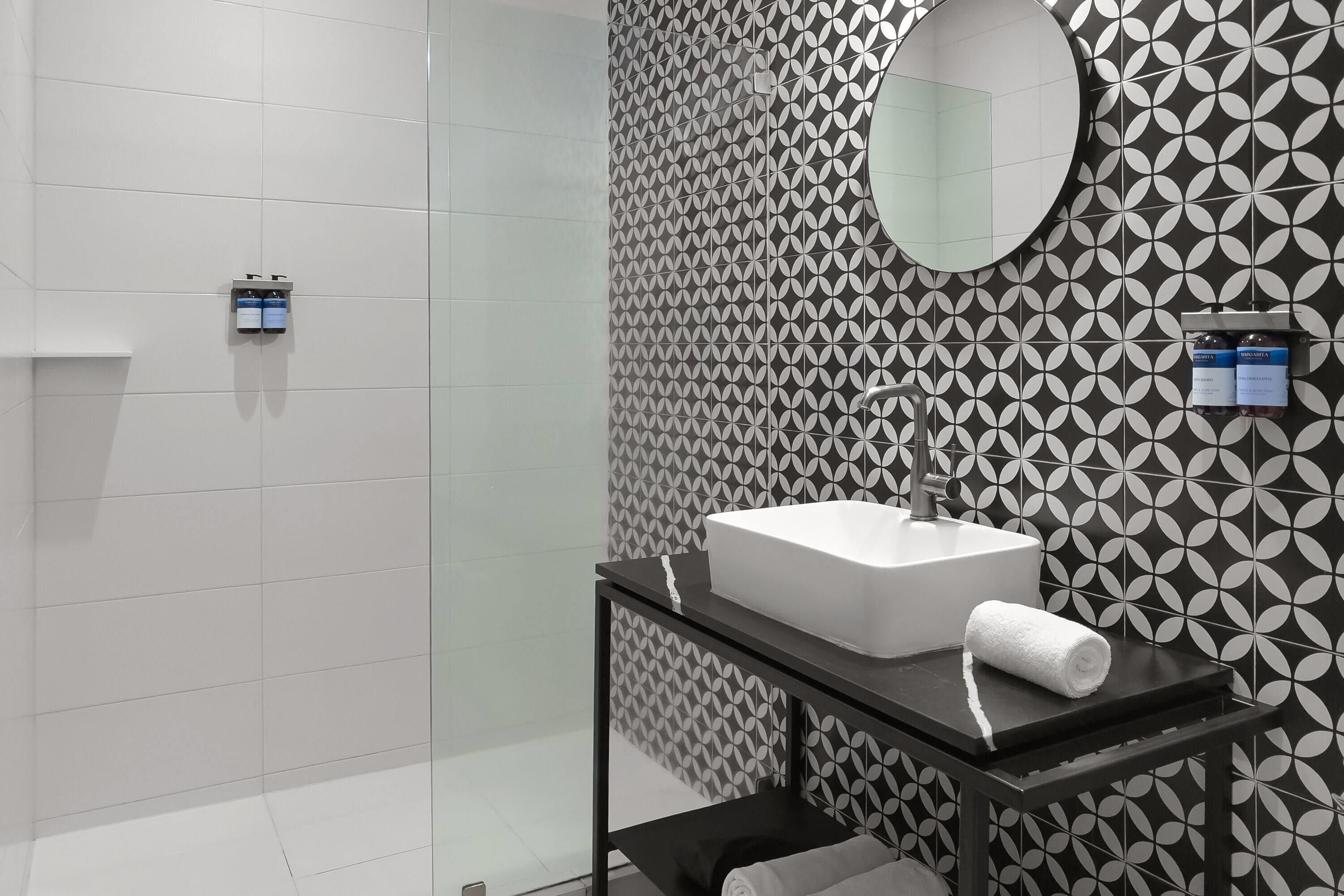 A modern bathroom with a white sink, a mirror, and patterned tiles.