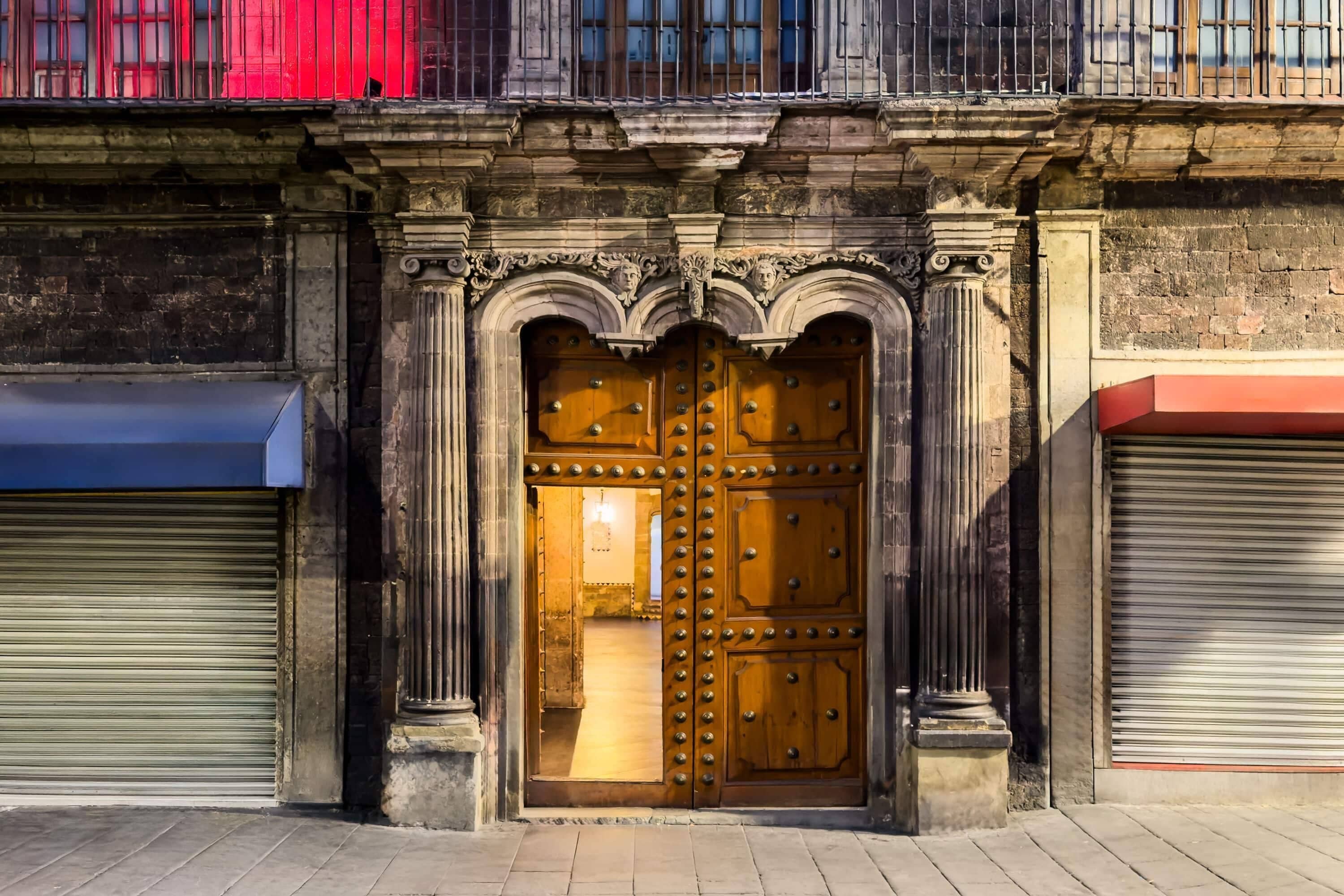 A large wooden door with ornate carvings and a metal grille, flanked by two closed shutters.