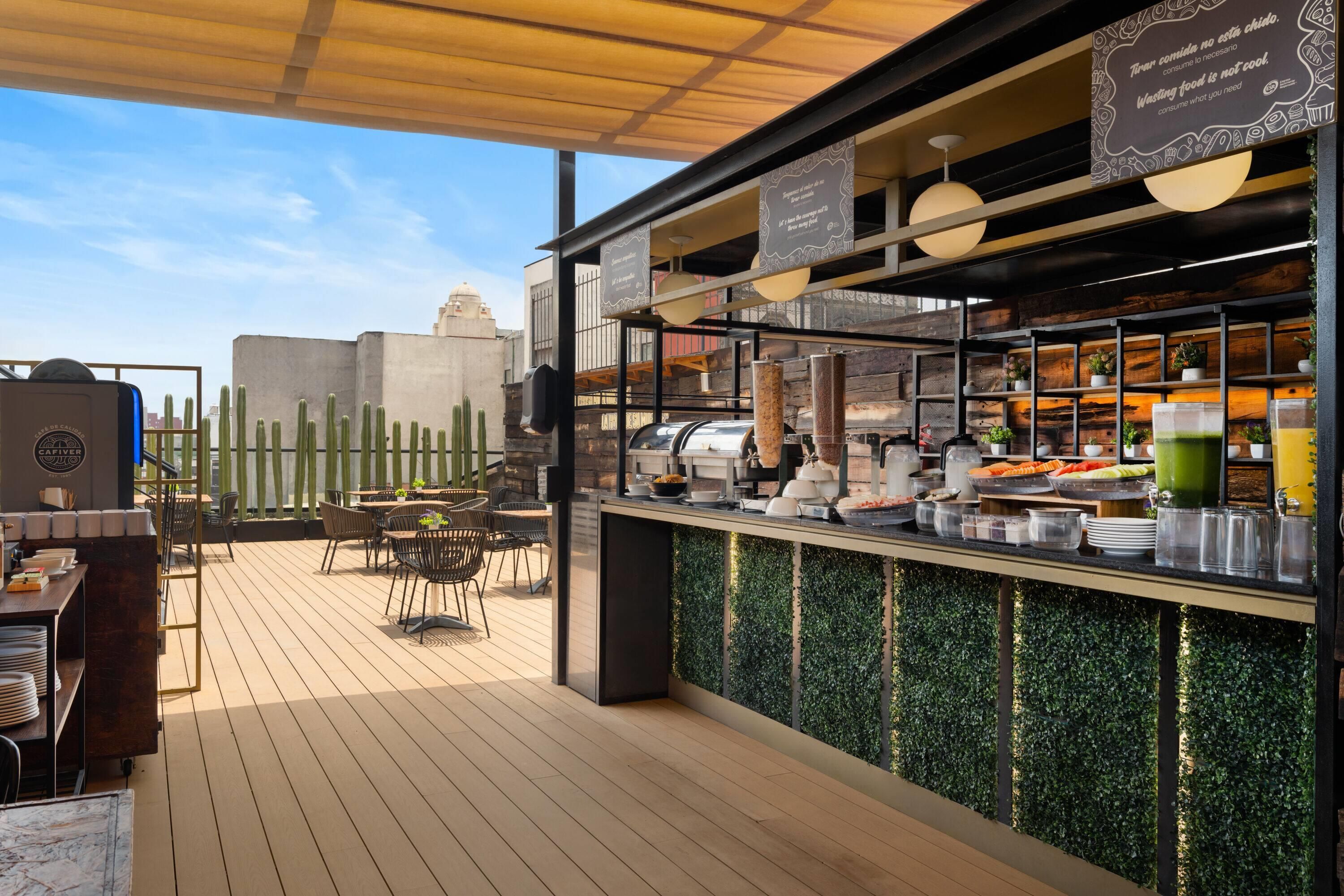 An outdoor café with a wooden deck, tables, chairs, and a buffet counter with various food items.