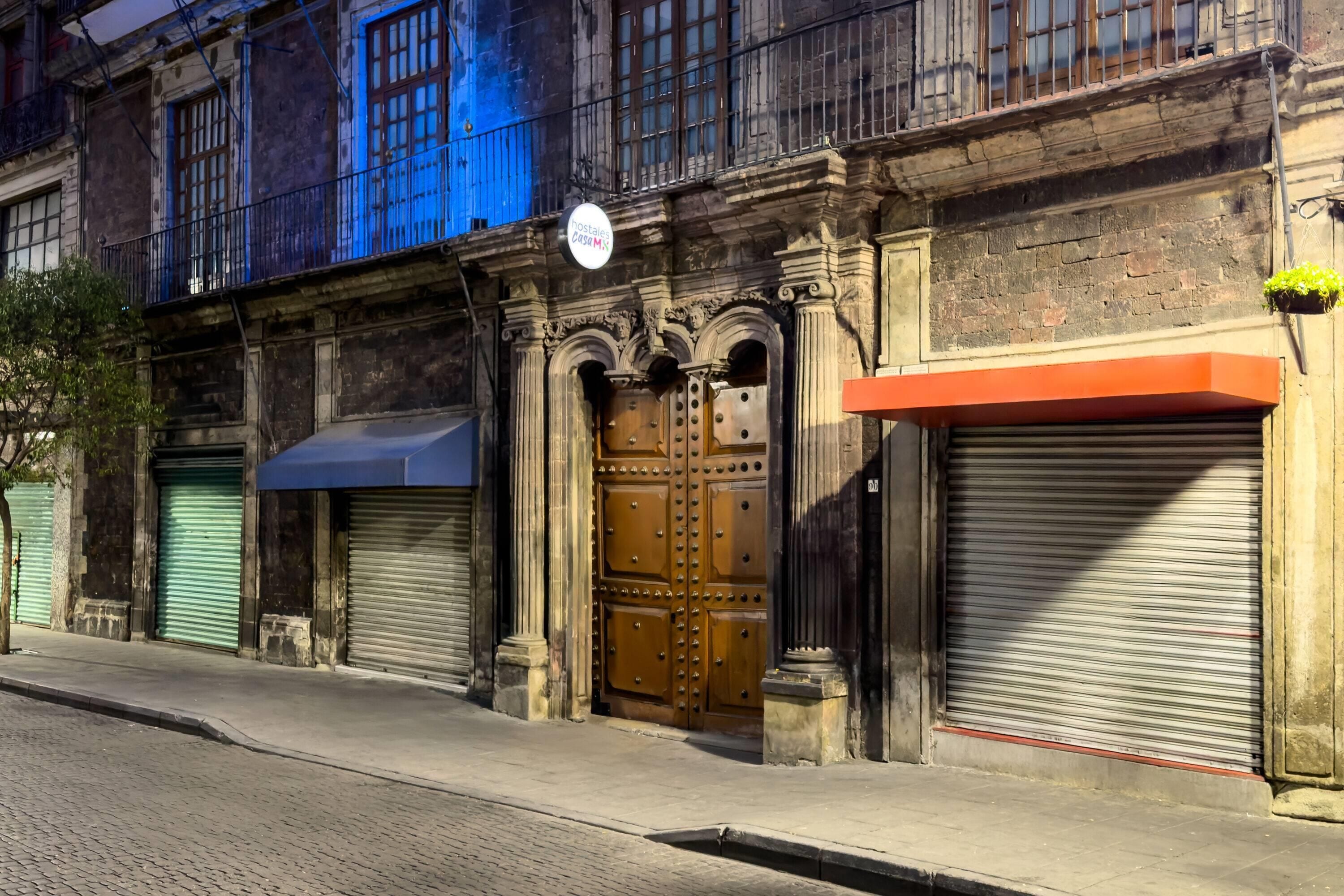 Um edifício com uma grande porta de madeira, uma marquise azul e uma placa acima da porta.