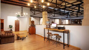 A spacious room with a wooden floor, a leather sofa, a small table, and a bar area with stools. - Hotel MX mas centro CDMX, Trademark Collection by Wyndham (Mexico City)