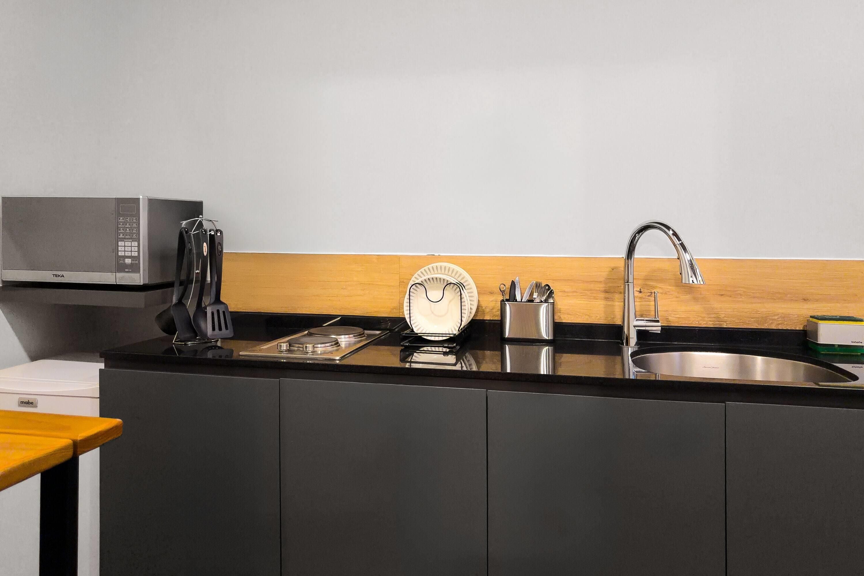 Una cocina moderna con microondas, estufa, pileta y utensilios.