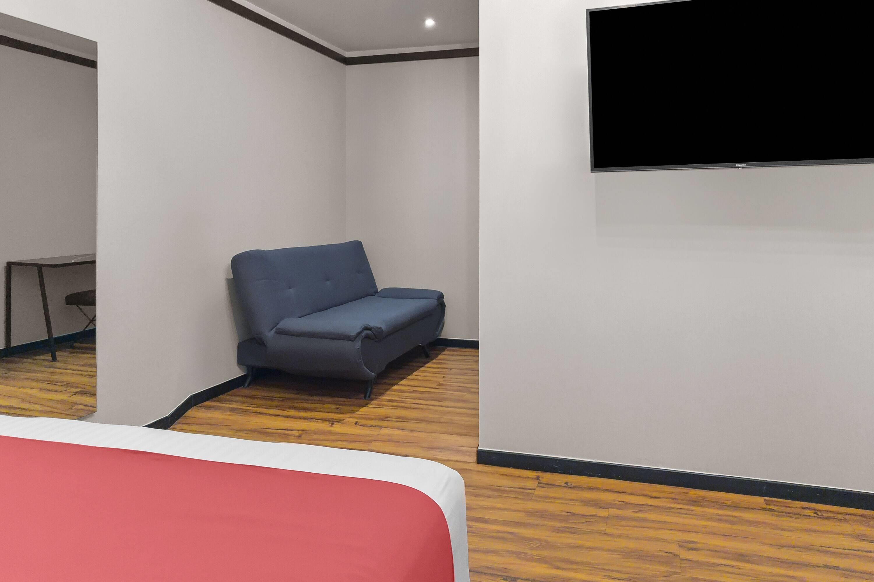 A room with a bed, a grey sofa, a television mounted on the wall, and a wooden floor.