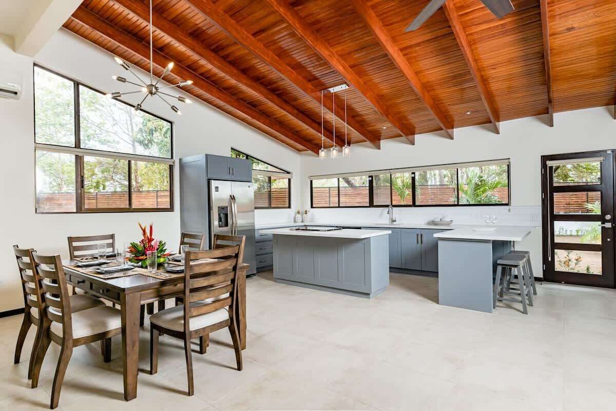 Una cocina amplia con una isla grande, vigas de madera en el techo y ventanas grandes que ofrecen vistas al verdor.