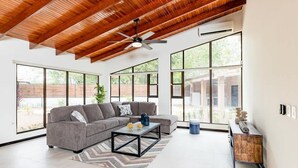 A spacious living room with a wooden ceiling, large windows, a gray sectional sofa, a coffee table, and a side table with decorative items. - Flamingo Estates 18- 4 BR House with Pool (Flamingo)
