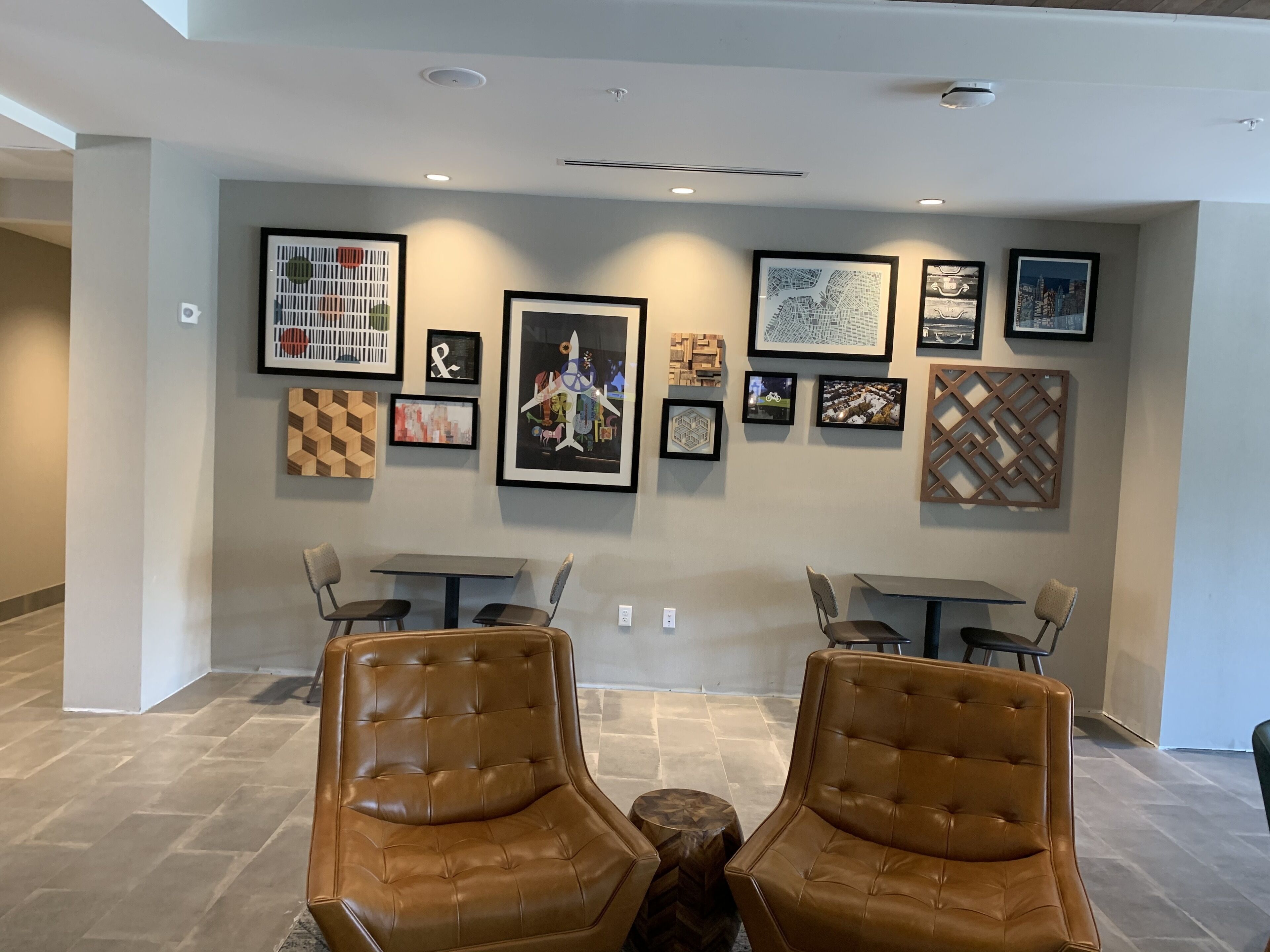Un intérieur moderne avec un coin salon comprenant deux fauteuils en cuir et une table, un mur orné de divers tableaux encadrés et un plafond doté d’un éclairage encastré.