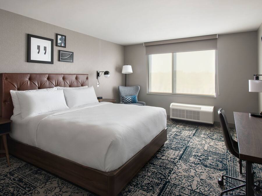 A hotel room with a large bed, a desk, a chair, and a window.