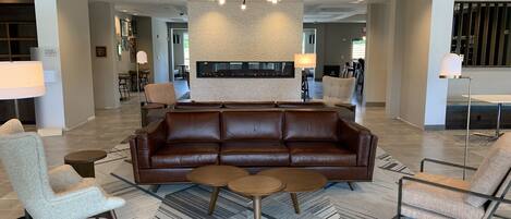 A spacious lobby with a leather sofa, round coffee tables, and a modern chandelier.