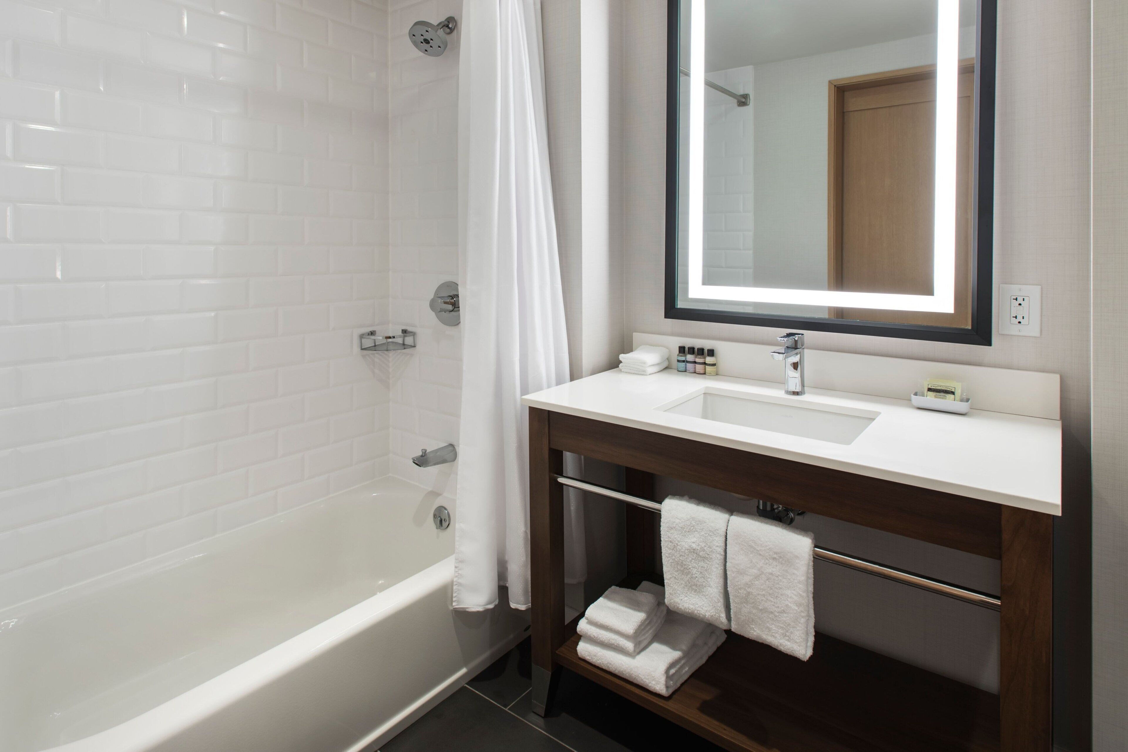 Une salle de bain moderne avec une baignoire blanche, un grand miroir et un meuble-lavabo doté d’un évier et d’un porte-serviettes.