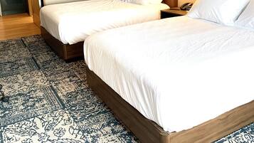 Hotellihuone, jossa on kaksi sänkyä, kuviollinen matto ja seinään kiinnitetyt valaisimet.