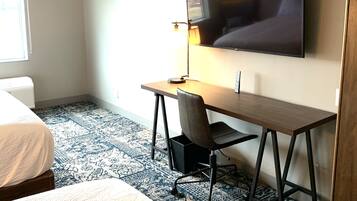 A hotel room with a bed, a desk with a chair, a television mounted on the wall, and a patterned carpet.