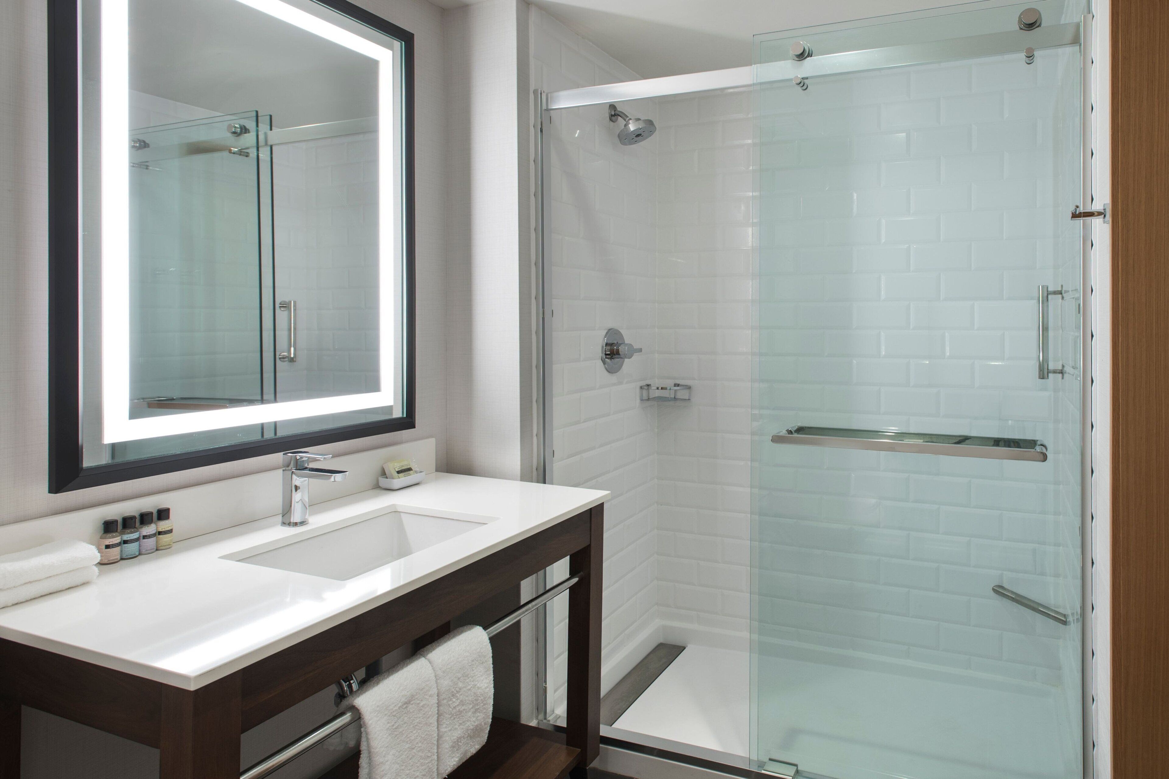 A modern bathroom with a glass-enclosed shower, a large mirror, and a white sink.