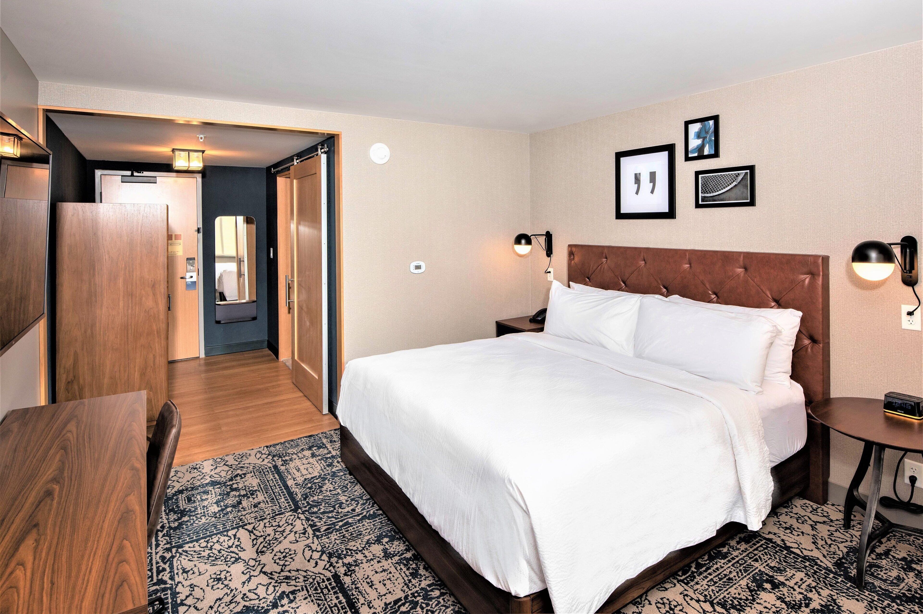 A hotel room with a large bed, a wooden wardrobe, a desk, and a small table.