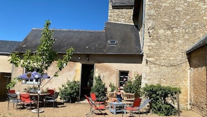 Ein Steinhaus mit einer Terrasse, die Gartenmöbel und einen kleinen Baum zeigt.