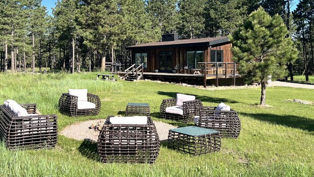 Una cabaña con mobiliario exterior y una terraza, rodeada de altos pinos.