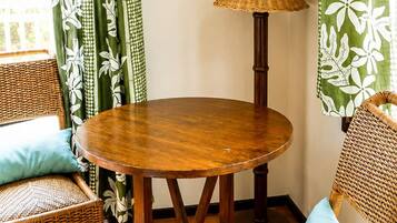 A room with a round wooden table, two wicker chairs, a hanging plant, and green patterned curtains.