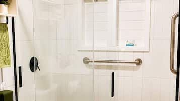 A bathroom with a glass-enclosed shower, a toilet, and a towel on the floor.