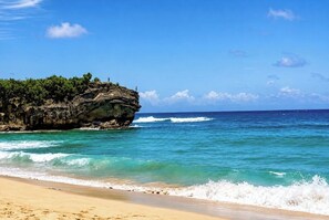 A beach with clear turquoise water, a sandy shore, and a rocky outcrop with vegetation. - An Affordable Alternative to Expensive Accommodations in Poipu (Poipu)