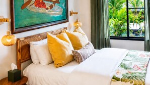A hotel room with a bed, a painting of a tropical scene, a window with curtains, and a view of greenery outside. - An Affordable Alternative to Expensive Accommodations in Poipu (Poipu)