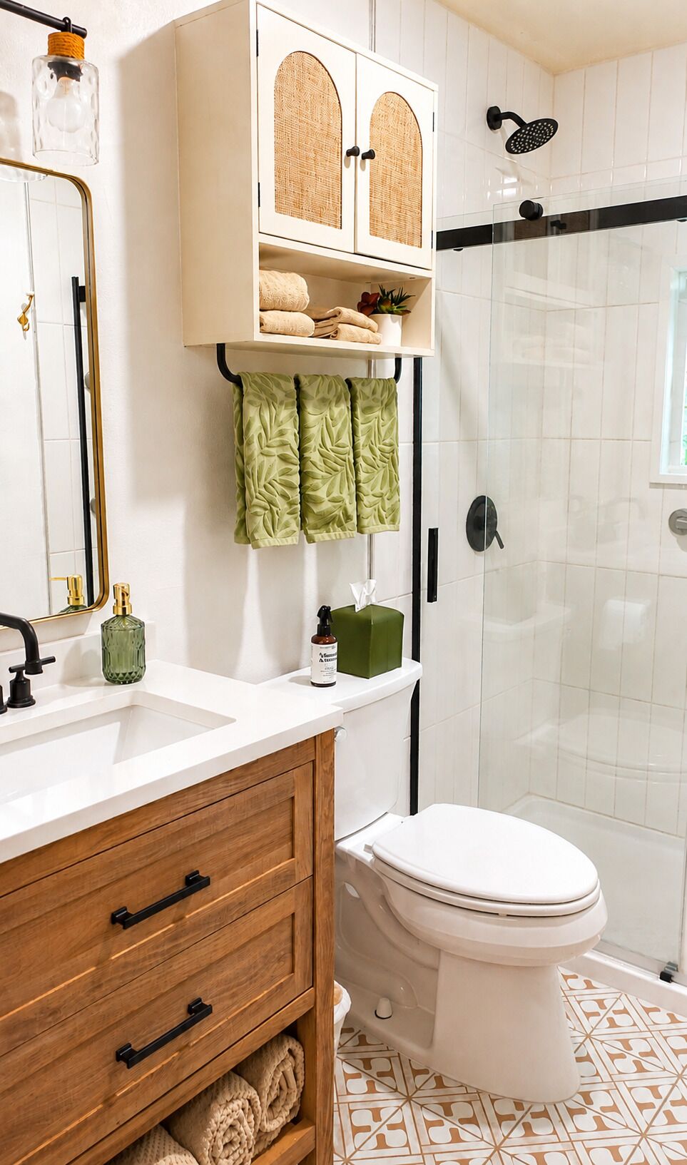 Un baño con inodoro blanco, lavabo con tocador de madera, ducha con puerta de vidrio y espejo con lámpara colgante.