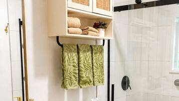 Un baño con inodoro blanco, lavabo con tocador de madera, ducha con puerta de vidrio y espejo con lámpara colgante.