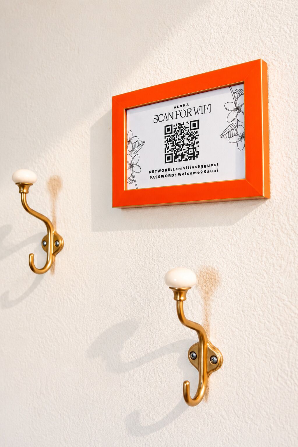 Een aan de muur bevestigde QR-code voor WiFi-toegang, twee messing wandhaken en een lijst met een QR-code.