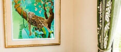 Una habitación con un sofá gris, un cuadro enmarcado de un leopardo y una cortina verde con estampado.