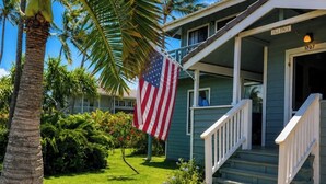 A two-story house with a porch, a flag, and a well-maintained lawn. - An Affordable Alternative to Expensive Accommodations in Poipu (Poipu)
