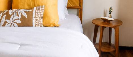 A neatly made bed with a floral comforter, a wooden headboard, and a small wooden nightstand with a lamp.