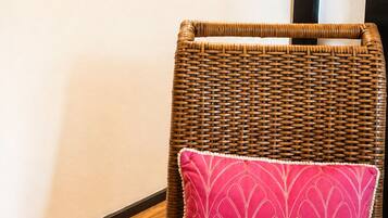A wicker chair with a pink cushion in a room with three framed pictures on the wall.