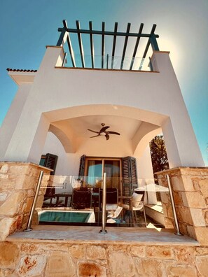 Een moderne villa met een zwembad, stenen muren en een balkon met een pergola.