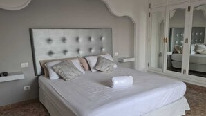 A neatly made bed with a tufted headboard, a bedside table, and a wardrobe with a mirrored door. - Happy Family Villa (Arucas)