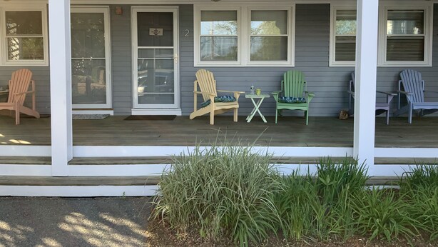 En veranda med Adirondack-stolar, ett litet bord och en dörr med skylten ”HOBBY”.