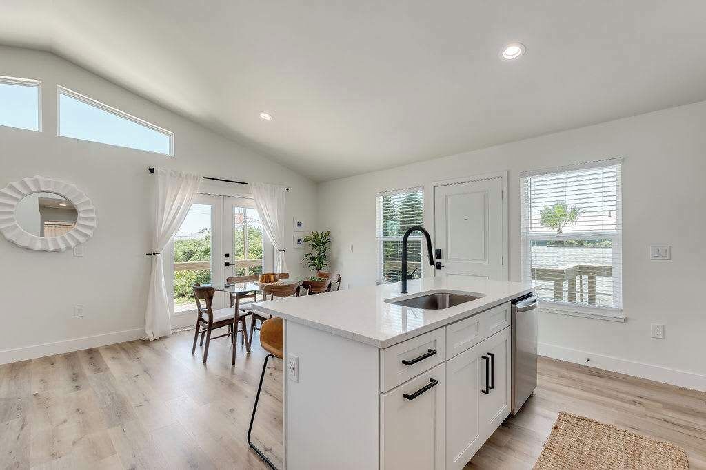 A modern kitchen with a white island, a sink, and a dining area with a table and chairs.