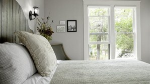 A bedroom with a large bed, a window with a view of trees, and a wall-mounted light fixture. - Historic Neighborhood 2 Blocks from Downtown Bozeman. (Bozeman)