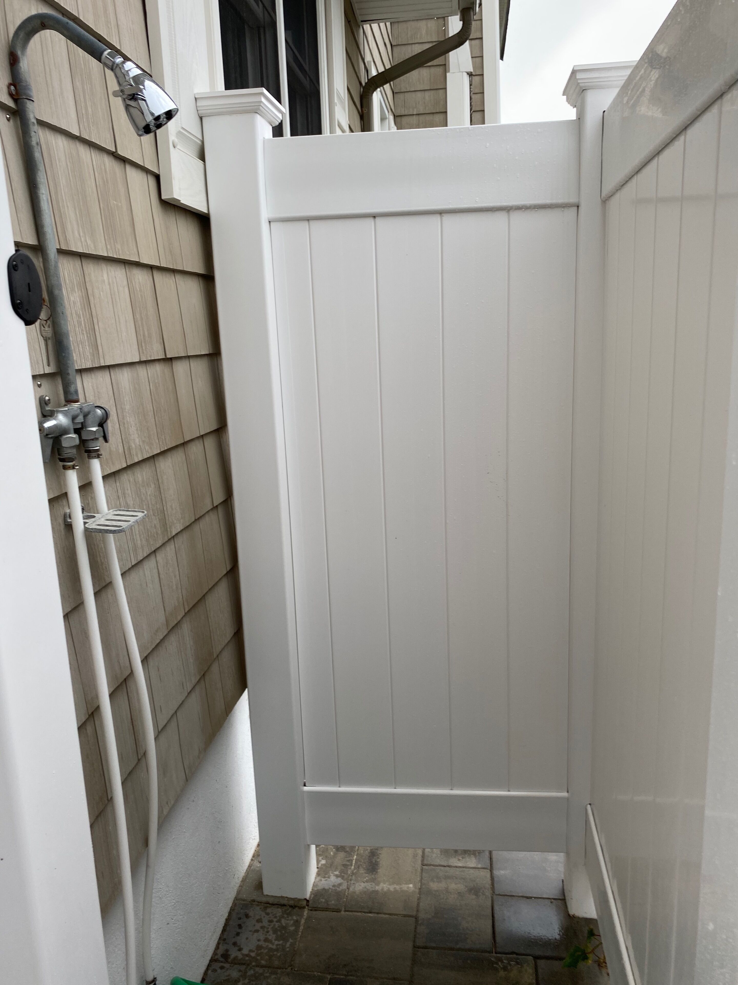 A white wooden gate leading to a small outdoor area with a metal hose and a faucet.