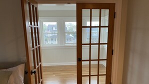 A room with a wooden door, a bed with white bedding, and a view of the outside through a window. - Beautiful, family friendly Bradley Beach home 1.5 blocks from the beach! (Bradley Beach)