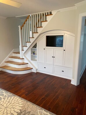 A staircase with wooden steps and white railings, leading to a white storage unit with a television.