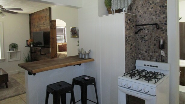 A compact kitchen with a gas stove, two stools, a wooden countertop, and a stone backsplash. - The Hideaway (Great Bend)