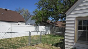 A fenced backyard with a white house, a wooden fence, and a tree. - The Hideaway (Great Bend)