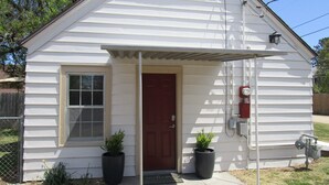 A small, single-story house with a red door, a window, and two potted plants. - The Hideaway (Great Bend)