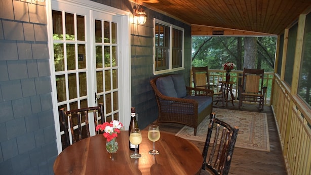 A covered outdoor dining area with a wooden table, chairs, and a wicker sofa. - Waterfall Cottage within sight & sound of Cane Creek Falls, 2BR 2BA (Dahlonega)