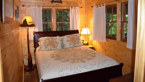 A cozy wooden cabin bedroom with a bed, two bedside lamps, and curtains. - Waterfall Cottage within sight & sound of Cane Creek Falls, 2BR 2BA (Dahlonega)